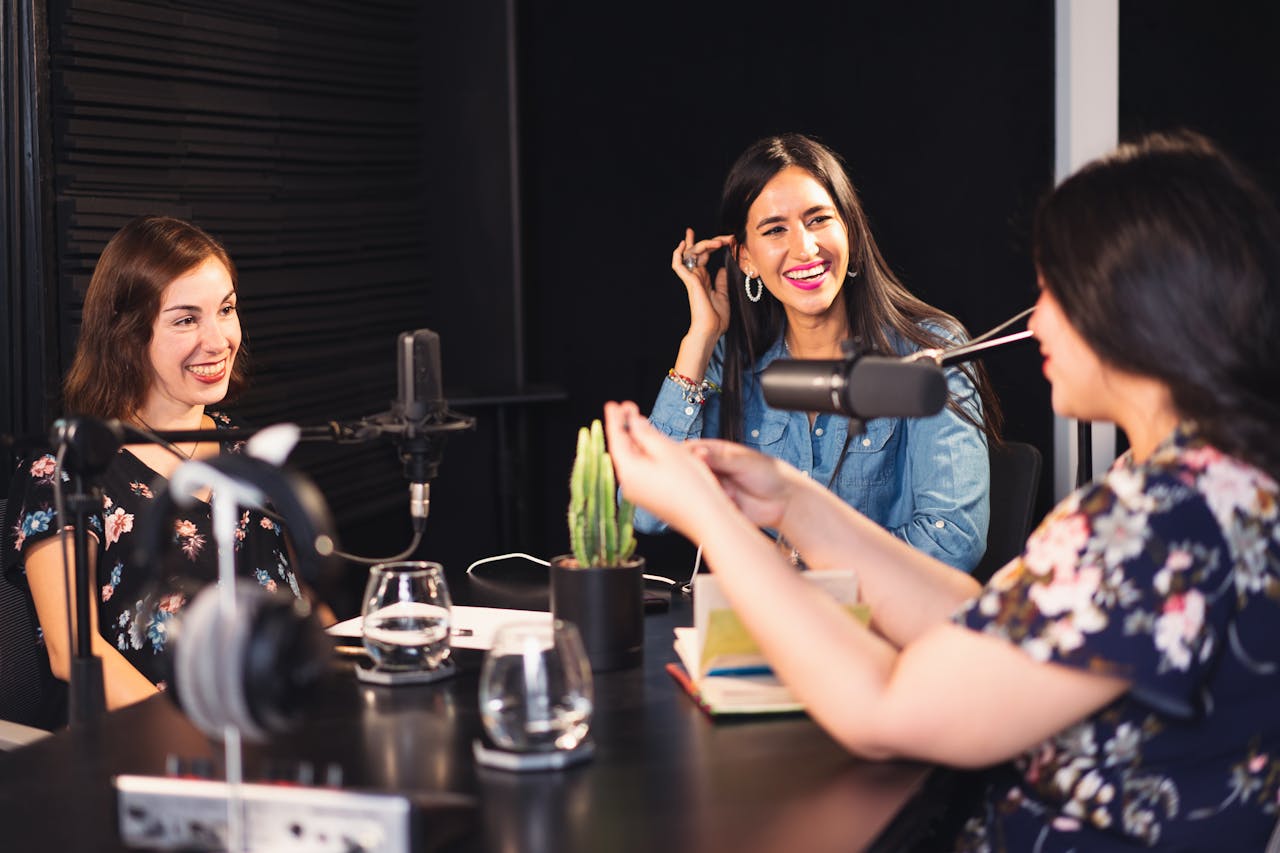 Three women enjoying a lively podcast discussion in a professional studio setting.